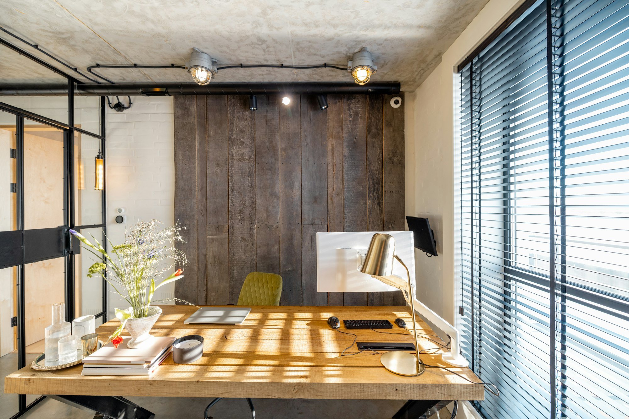 Home office with a rustic timber desk, dark timber feature wall and steel-framed glass