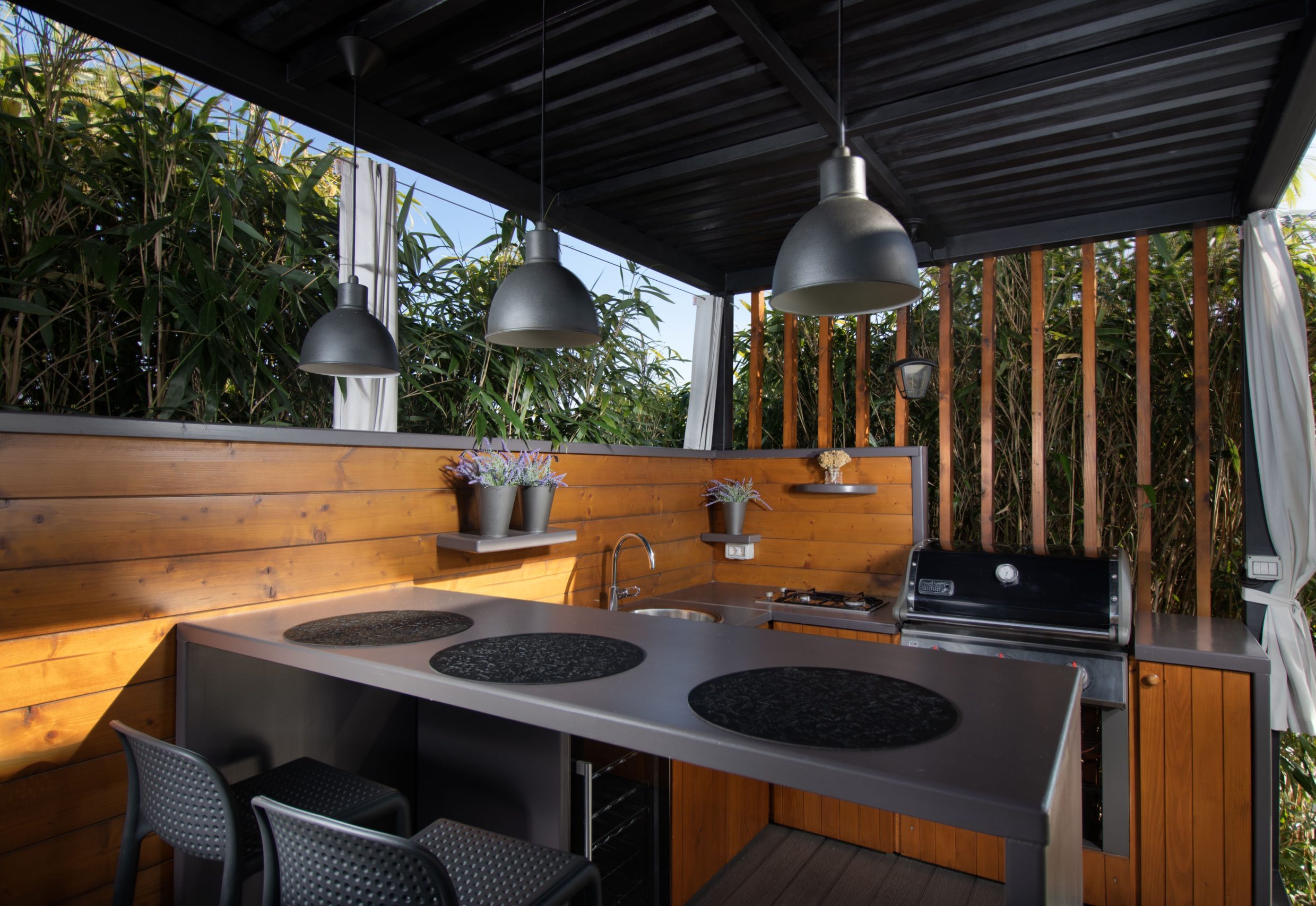 Outdoor kitchen with a dark benchtop, barbecue and timber cabinets under a pergola
